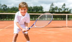 ラケット持ってコートに立つ可愛い男子ジュニアテニスプレーヤー