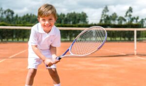 ラケット持ってコートに立つ可愛い男子ジュニアテニスプレーヤー