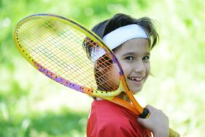 テニスラケットを持って笑うジュニアテニスプレーヤー